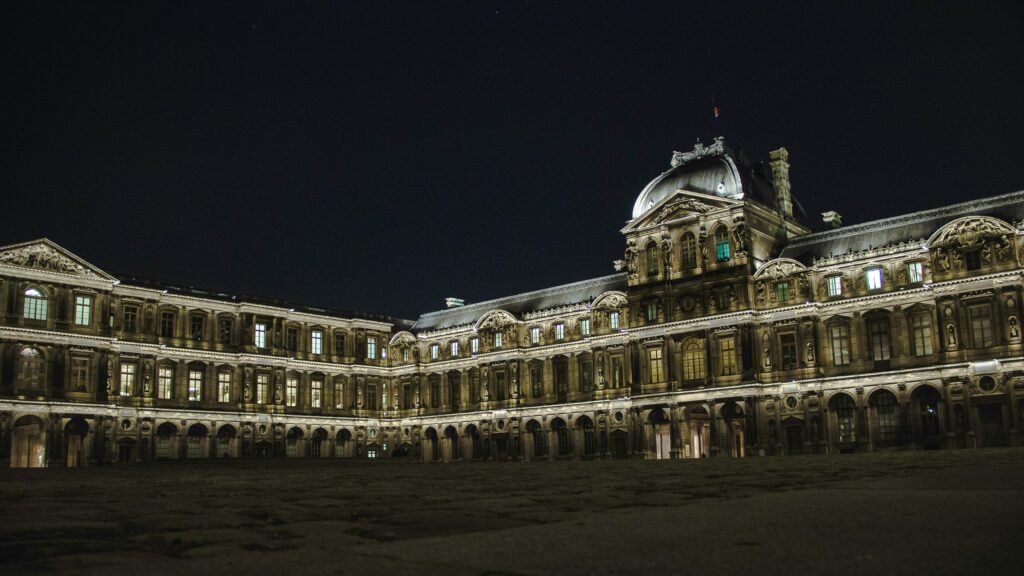 Dramatic architectural night shot of the Louvre Palace in Paris, featuring baroque elegance.
